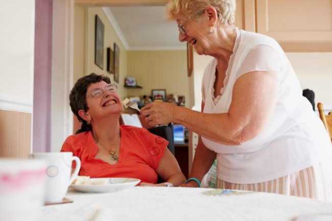 carer helping a woman with a disability to eat a meal
